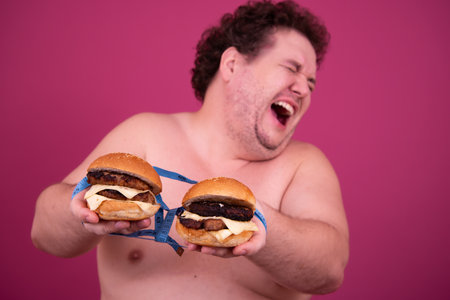 Fat man with hamburgers in hands on a pink background.の写真素材