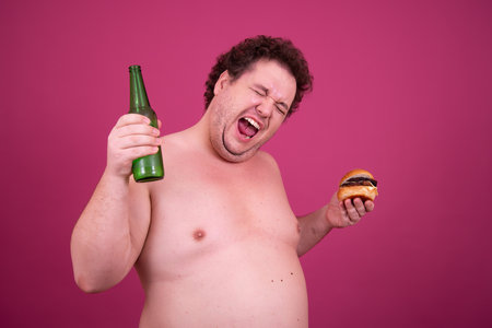 Fat man with a hamburger and a bottle of beer on a pink backgroundの写真素材