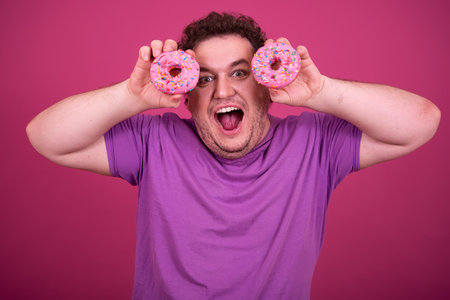 Portrait of happy overweight bearded man holding donuts against pink backgroundの写真素材