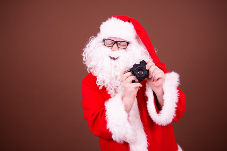 santa claus taking photos with a camera on a brown backgroundの写真素材