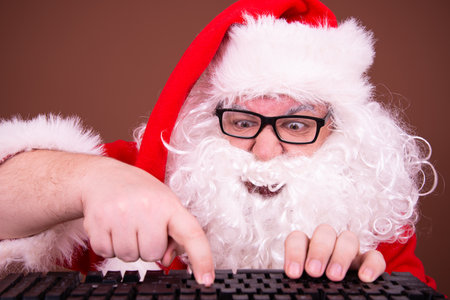 Portrait of happy Santa Claus sitting at table and typing on keyboardの写真素材