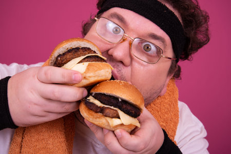 Funny fat man eating hamburger, isolated on pink background.