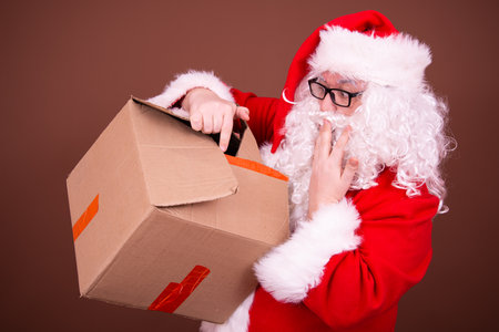 Studio shot of Santa Claus against brown background while holding a cardboard boxの写真素材