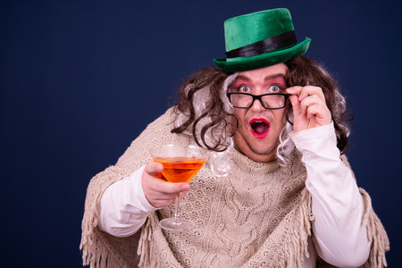 Portrait of a funny leprechaun holding a glass of martini against blue backgroundの写真素材