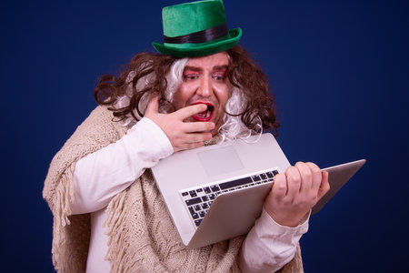 Funny leprechaun man with laptop computer on blue backgroundの写真素材