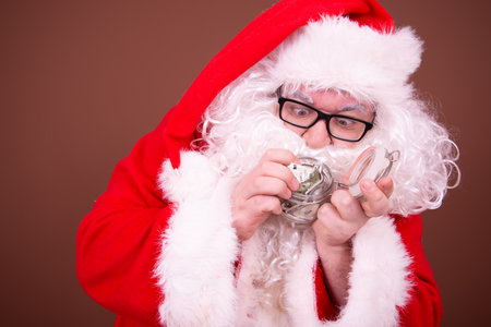 Portrait of santa claus with piggy bank against brown backgroundの写真素材
