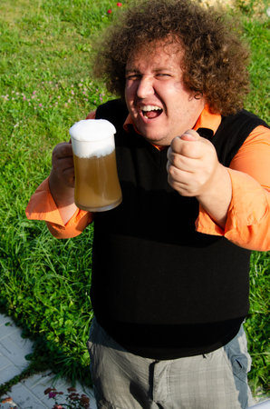 Young man with curly hair drinking beer and showing thumbs up in the parkの写真素材