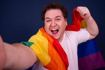 Funny young man with a rainbow flag on a blue background.の写真素材