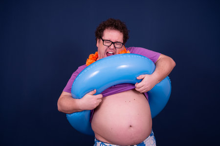 Fat man with an inflatable ring on his stomach against blue backgroundの写真素材