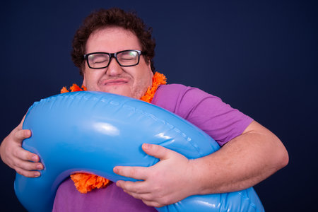 Portrait of a funny man holding inflatable ring against blue backgroundの写真素材