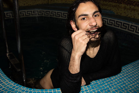 An attractive guy with long hair is relaxing in the pool. Relaxation and pleasure.の写真素材