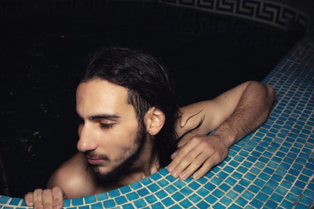 An attractive guy with long hair is relaxing in the pool. Relaxation and pleasure.