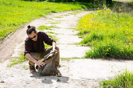 Man sitting on a dirt road with a backpack and looking at the cameraの写真素材