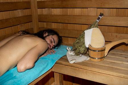 An attractive guy with long hair is relaxing in the sauna. Relaxation and pleasure.の写真素材