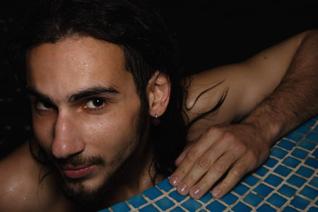 An attractive guy with long hair is relaxing in the pool. Relaxation and pleasure.
