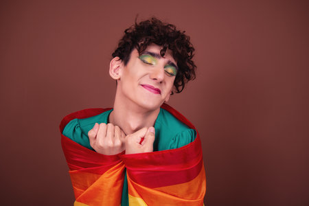 Portrait of a young woman wrapped in a rainbow flag against brown backgroundの写真素材