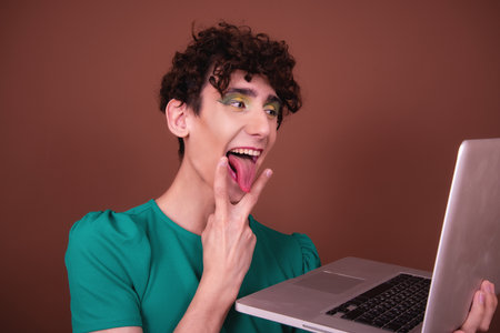 Portrait of a funny young man using laptop computer isolated on brown backgroundの写真素材