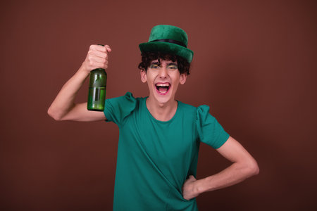 Young handsome man wearing green shirt against brown background with leprechaun hatの写真素材