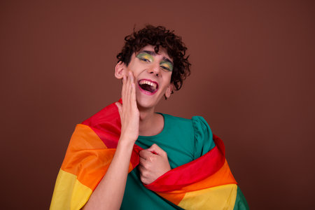 Portrait of a young woman with curly hair and rainbow flag against brown backgroundの写真素材