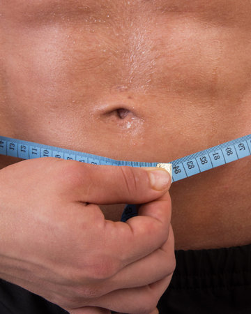 Man measuring his waist with a measuring tape. Close-up.