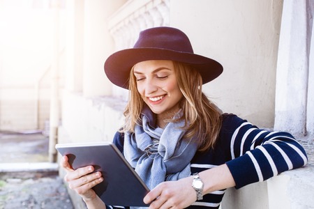 Attractive young female tourist chatting with colleagues talking about her adventure abroad while standing on cityscape on sunny day using tablet gadget.の写真素材