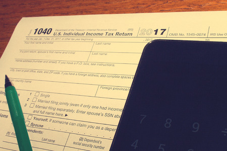 Tax day. The tax form 1040, green pen and black smartphone with calculator is on a wooden table.の写真素材
