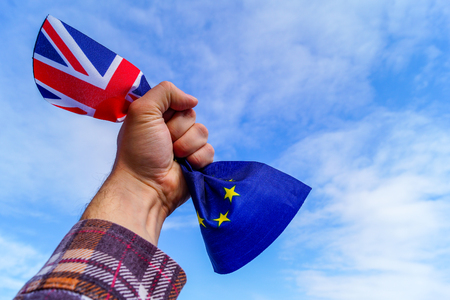 A male hand holds in his fist the flags of England and the European Union against a blue sky and symbolizes Brexit or No Brexit. Image contains copy space.の写真素材