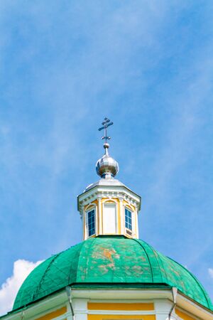 Yellow Orthodox Christian church with a green dome against a blue sky with white clouds.の写真素材