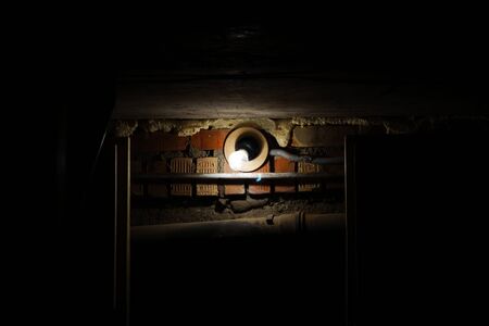 A light bulb shines on an old brick wall in a dark room.の写真素材