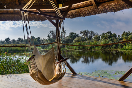 Chair hammock in the arbor on nature background. Peaceful view on the lake from wooden gazebo.の写真素材