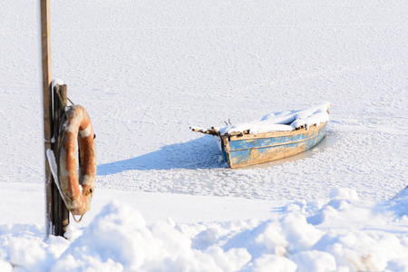 Old boat on ice. Winter landscape composition with old boat ice, snow, rescue seat.の写真素材