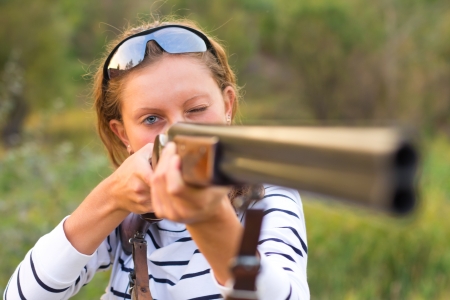 A young girl with a gun for trap shooting and shooting glasses aiming at a targetの写真素材