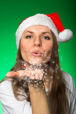 Girl in a Christmas hat blows off snowflakesの写真素材