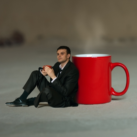 Concept  Businessman with a cup of tea sitting around a large cup in thoughtの写真素材