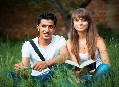 Two students guy and girl studying in park on grass with book outdoorsの写真素材