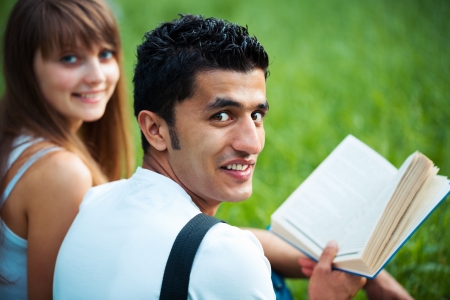 Two students guy and girl studying in park on grass with book outdoorsの写真素材