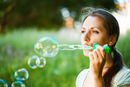 Close-up portrait of a girl blowing soap bubbles in the parkの写真素材