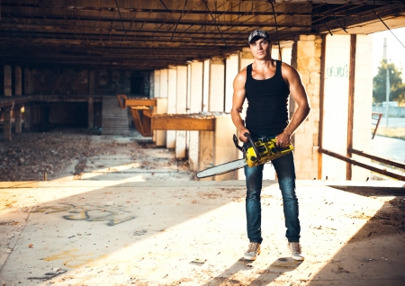 Muscular man with a chainsaw on the ruinsの写真素材