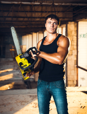 Muscular man with a chainsaw on the ruinsの写真素材