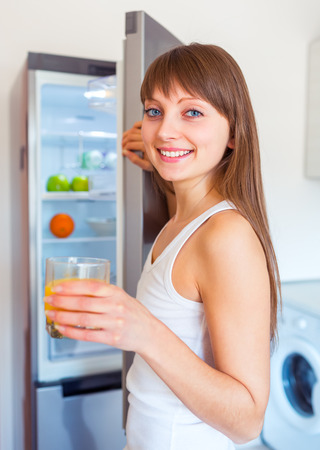 Young caucasian brunette girl with a glass of juice near the refrigeratorの写真素材