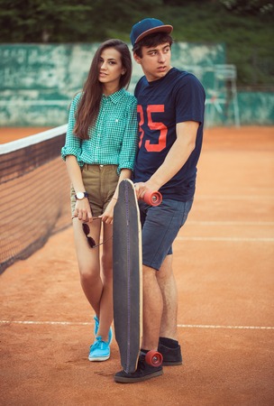 Young beautiful couple standing on a skateboard on the tennis courtの写真素材