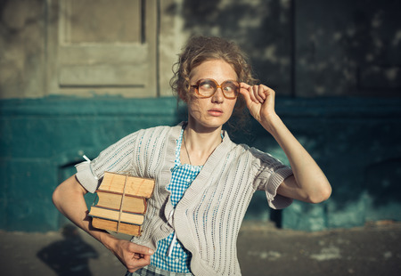 Funny girl student with books in glasses and a vintage dress outdoorsの写真素材