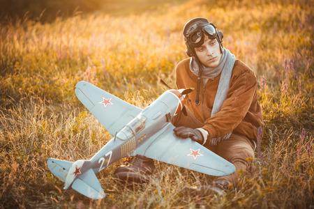 Young guy in vintage clothes pilot with an airplane model outdoorsの写真素材