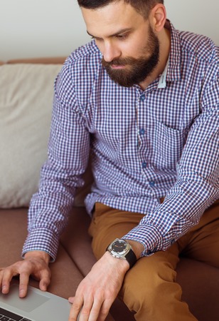 Young bearded man working on laptop at homeの写真素材