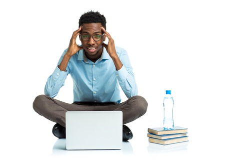 African american college student with headache sitting on white background with laptop and some booksの写真素材