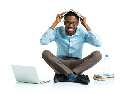 Happy african american college student with laptop, books and bottle of water sitting on white...