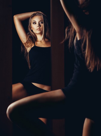 Beautiful sexy young woman looking into a mirror at herselfの写真素材