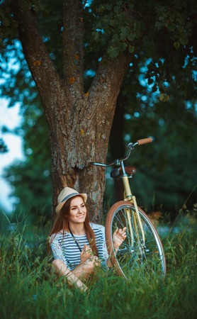 Lovely young woman in a hat with a bicycle in a park. Outdoorsの写真素材
