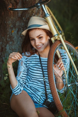 Lovely young woman in a hat with a bicycle in a park. Outdoorsの写真素材