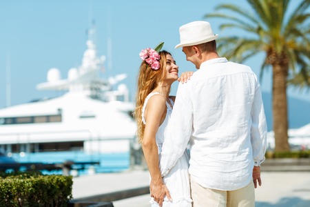 Attractive young couple walking alongside the marina with moored boats on a luxury waterfront in summer sunshineの写真素材